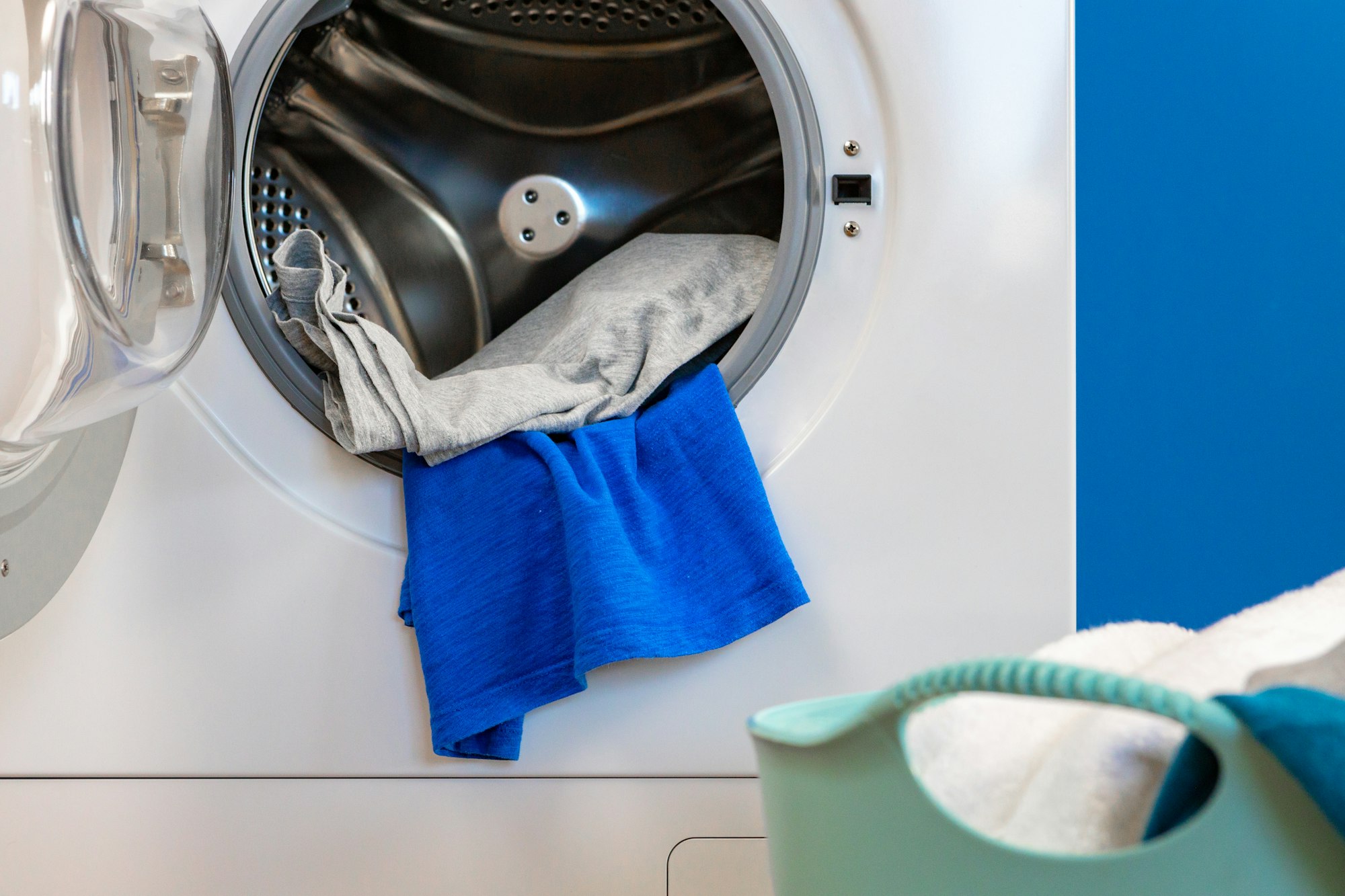 Washing machine with laundry on blue wall background